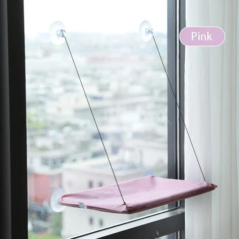 Pink cat hammock with suction cups installed on a window, providing an elevated, cozy resting spot.