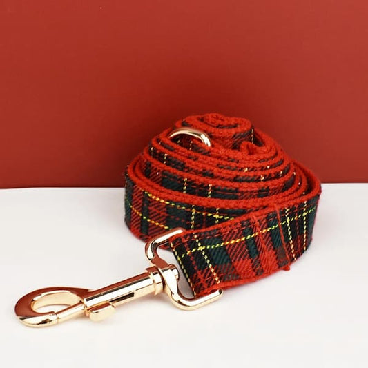 Red and black plaid dog leash with gold clip on a white surface against a red background