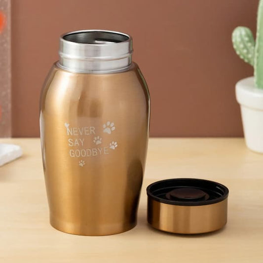 Gold urn with engraved text on a wooden surface with a cactus in the background