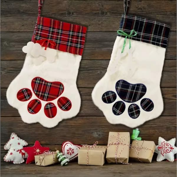 Two Christmas stockings with paw print designs on a wooden background with small gift boxes and decorative items.