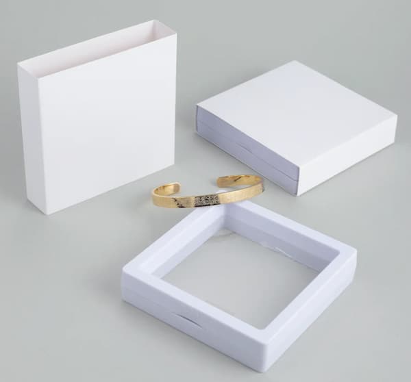 Gold bracelet on a white jewelry display box with a gray background