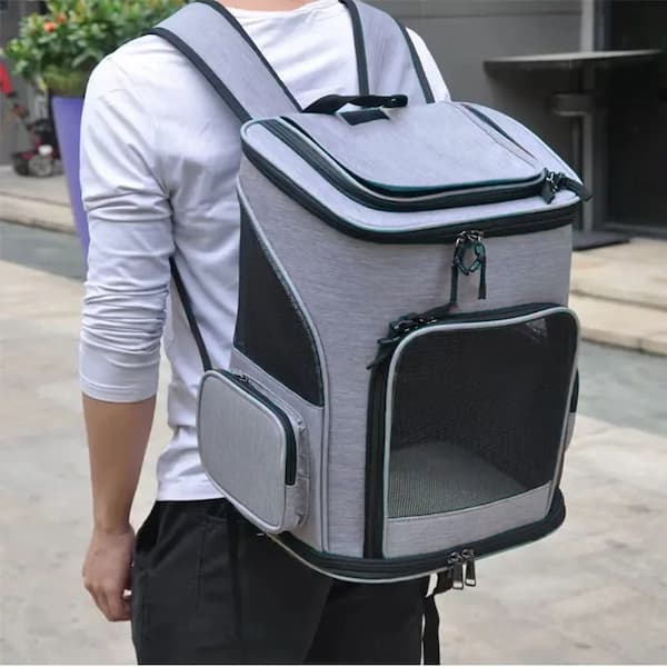 Person carrying a gray pet carrier backpack outdoors.