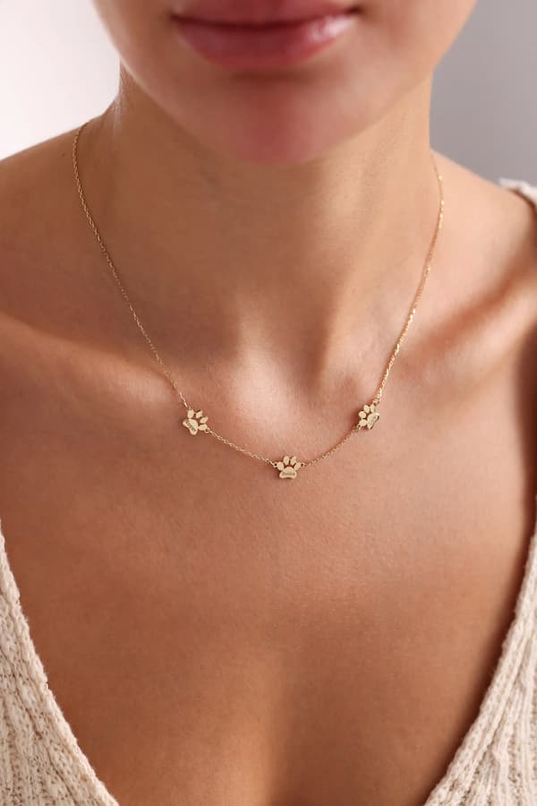 Gold necklace with paw print charms on a person wearing a beige top.