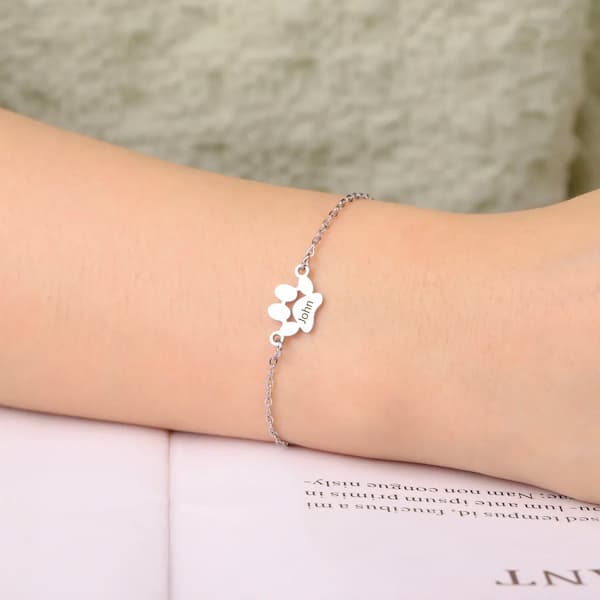 Silver bracelet with paw print design on a person's wrist against a neutral background