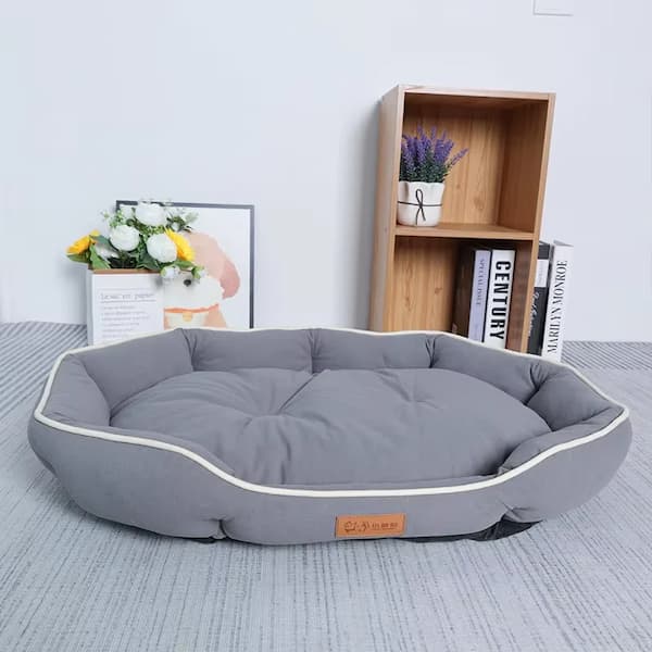 Gray pet bed on a gray floor with a wooden bookshelf in the background