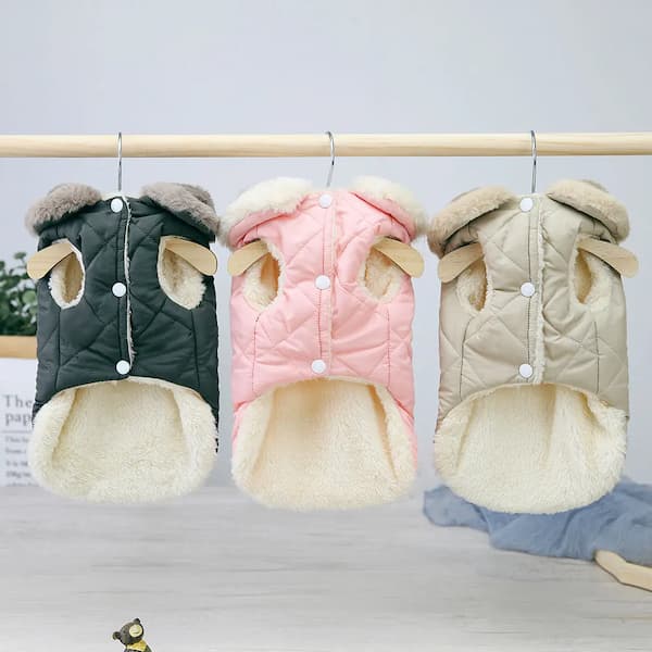 Three pet coats in black, pink, and beige hanging on a rack against a light gray background.