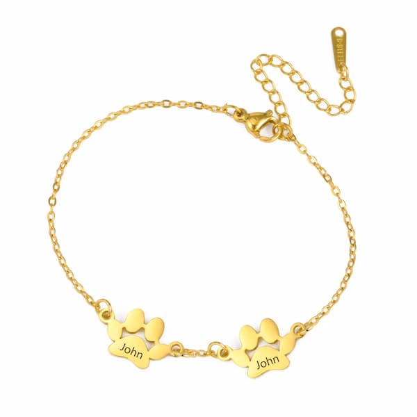 Gold bracelet with paw prints and 'John' engraving on a white background