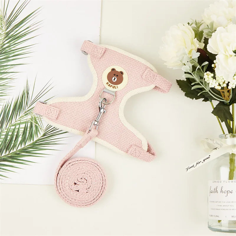 Pink pet harness with a bear design on a white surface with flowers and leaves.