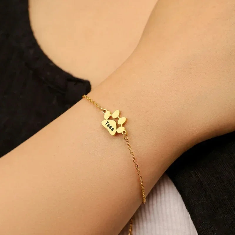 Gold bracelet with paw print design on a wrist against a neutral background