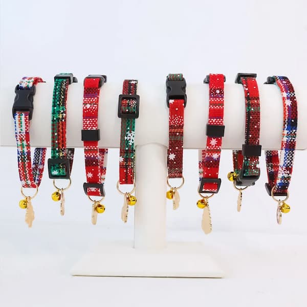 Set of red and green patterned pet collars with bells on a white stand.