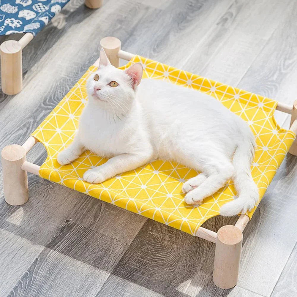 Modern wooden raised cat bed with yellow geometric fabric cushion and white cat, stylish pet furniture.