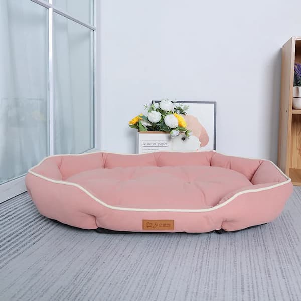Pink pet bed on a gray carpet with a light blue wall and window in the background.