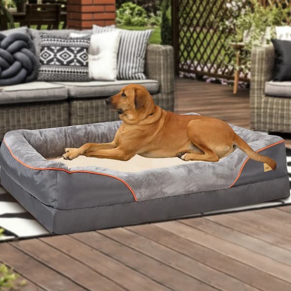 Dog lying on a large gray pet bed outdoors on a wooden deck.