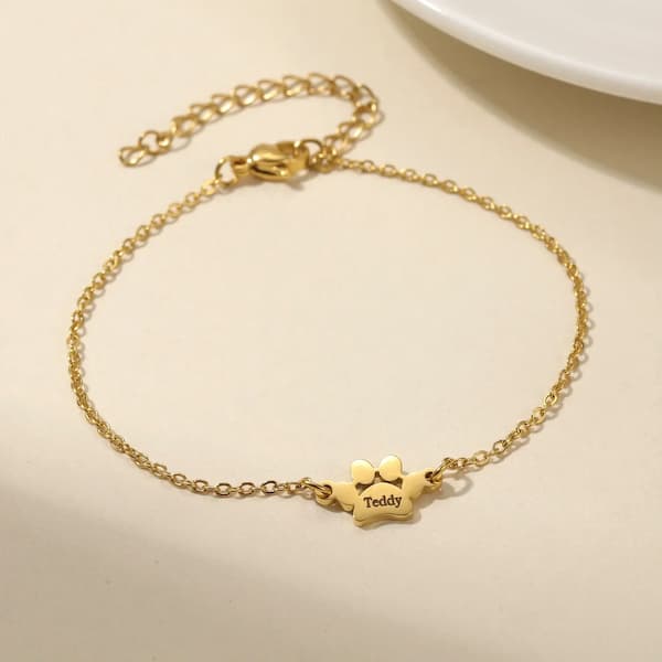 Gold bracelet with a paw-shaped charm on a beige surface