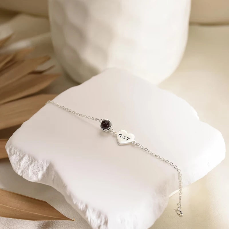 Silver bracelet with a heart-shaped charm and gemstone on a white stone surface.