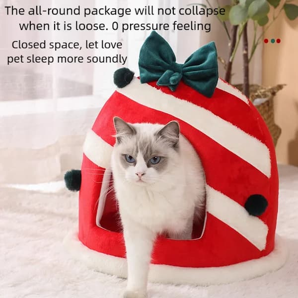 Cat inside a red pet house with a green bow, sitting on a soft surface.