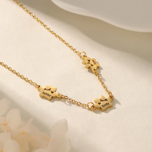 Gold necklace with paw-shaped charms engraved with names on a light background
