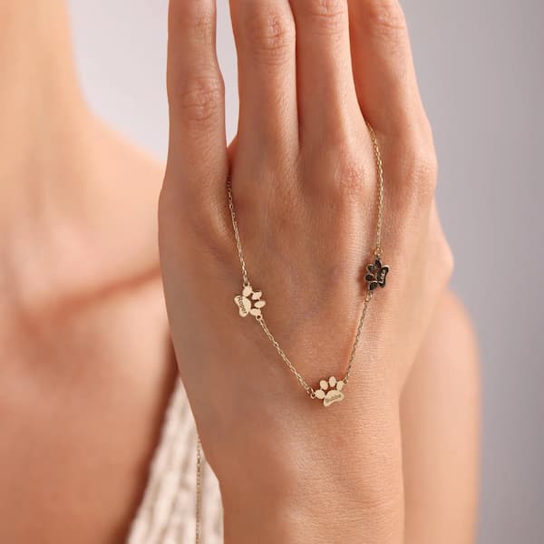 Gold paw print necklace on a hand against a neutral background