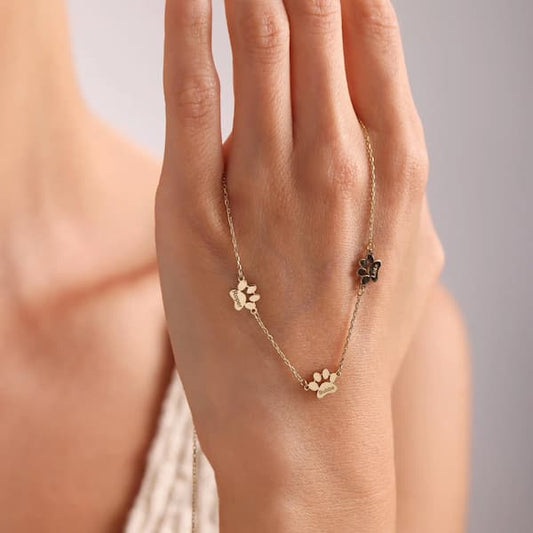 Gold paw print necklace on a hand against a neutral background