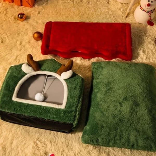 Green reindeer-shaped pet bed with red blanket on a carpeted floor.