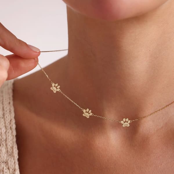 Gold necklace with paw print charms being worn on a person's neck.