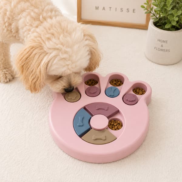 Curly-haired puppy using a pink paw-shaped interactive puzzle feeder designed to slow eating and provide mental stimulation for dogs