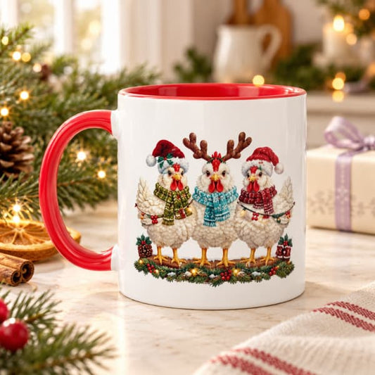 Red-handled Christmas mug featuring three festive chickens, styled with evergreen branches, fairy lights and a wrapped gift.