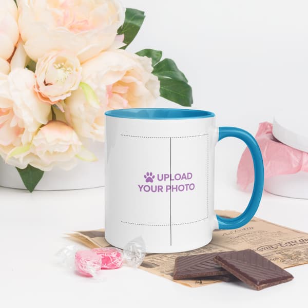 White mug with blue handle and interior, featuring text 'Upload Your Photo', placed on a surface with flowers and chocolate.
