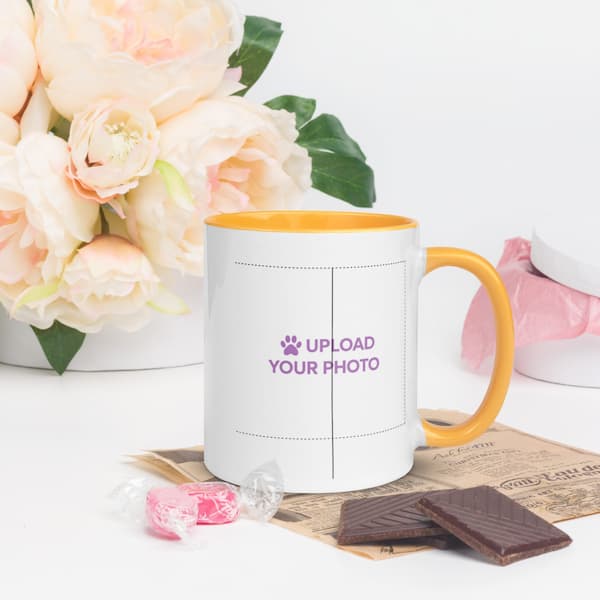 White mug with orange handle and rim, featuring text 'Upload Your Photo', on a white surface with flowers and chocolate.