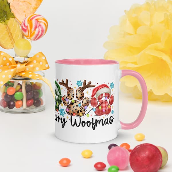 White mug with pink handle featuring a Christmas-themed design, surrounded by colorful candies and flowers.