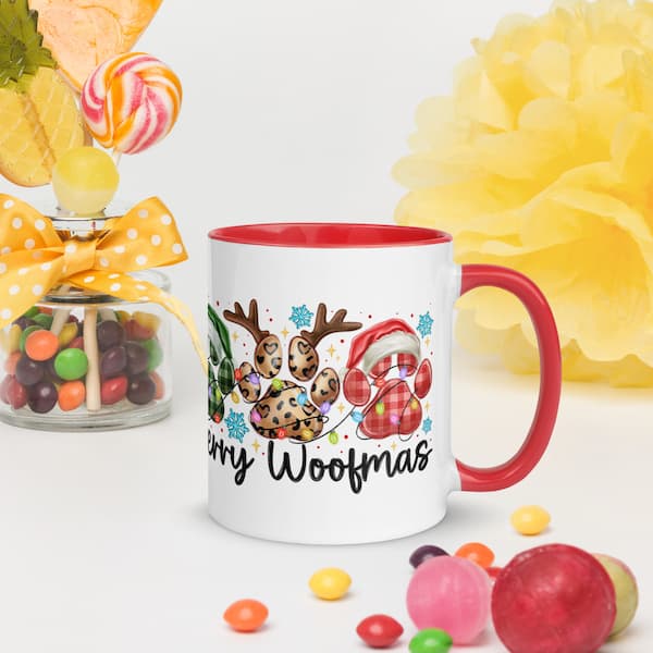 White mug with red handle featuring a Christmas design and 'Merry Woofmas' text, surrounded by colorful candies and flowers.