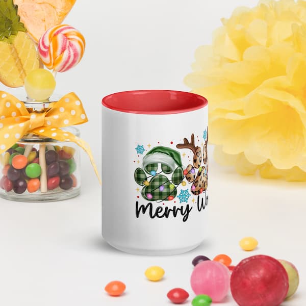 White mug with red interior, Christmas-themed design, and 'Merry Wreath' text, surrounded by colorful candies and a yellow decorative item.