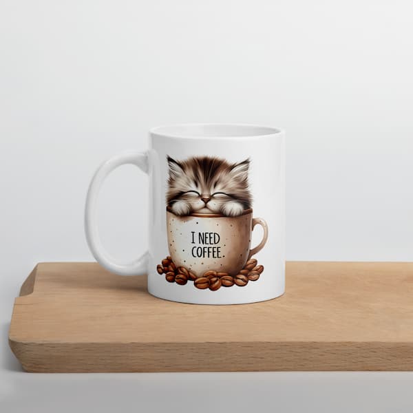 White mug with a cat illustration and 'I Need Coffee' text on a wooden surface.