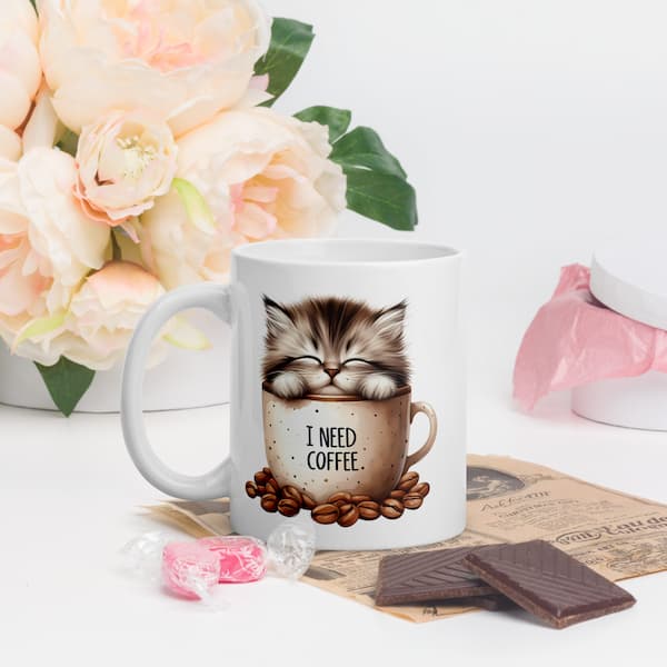 Cute fluffy kitten sleeping inside a coffee mug with the words “I Need Coffee” surrounded by coffee beans – ceramic cat lover gift mug.