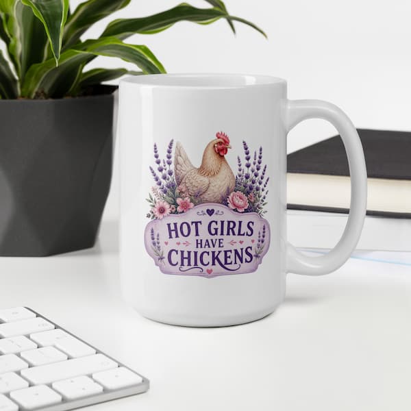 White mug with a chicken design and Hot girls have chickens written on, on a desk with a plant and keyboard in the background
